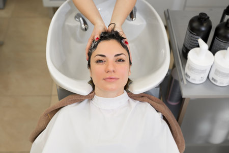 Young girl hairdresser washes her hair with shampoo and massages the head of a young woman in a...