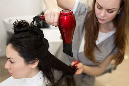 Portrait of a woman hairdresser who works with a client in a beauty salon. Hairdresser dries wet hair girl with a hair dryer.の写真素材