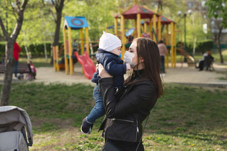 Young girl in a protective mask kisses her little child. Covid-19.の写真素材