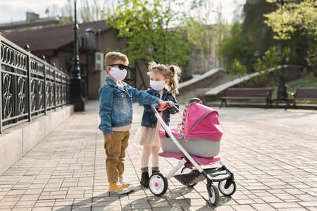 Boy and a girl walk with a pram in protective face masks. Concept of family. Coronavirus, covid-19.