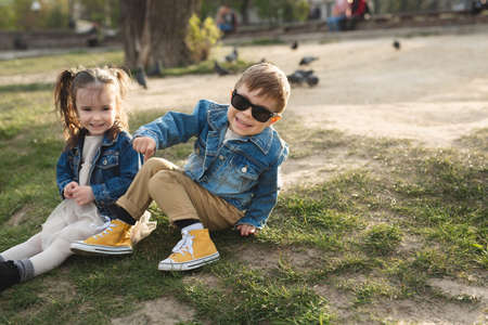 A little happy cute boy and a little cute girl sitting on the grass in a beautiful place.