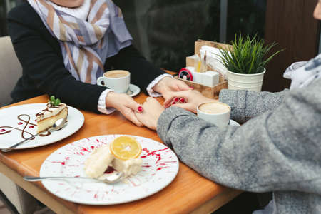 Close-up of a mother and daughters hands on a wooden table in a cafe. Adult mother and daughter hold hands and drink coffeeの写真素材