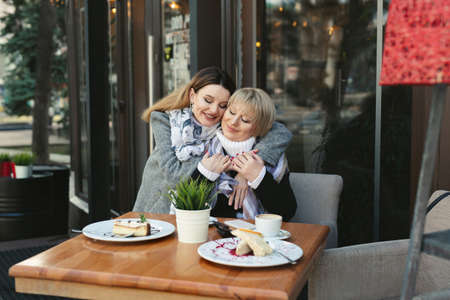 Elderly woman and her adult daughter hug and kiss in a cafe on the street. Emotion of loveの写真素材