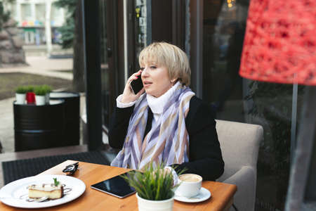 Old woman is talking on the phone during lunch in a cafeの写真素材