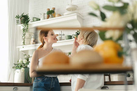 An adult daughter feeds her elderly mother fresh pastries in the kitchenの写真素材