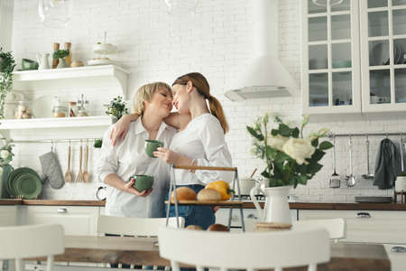Portrait of a happy elderly mother and daughter in the kitchen, they drink tea and enjoy a conversation. Tender portrait of an old mother with an adult daughter at home.の写真素材