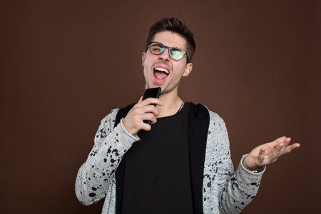 A young man sings into his phone on a brown background.の写真素材