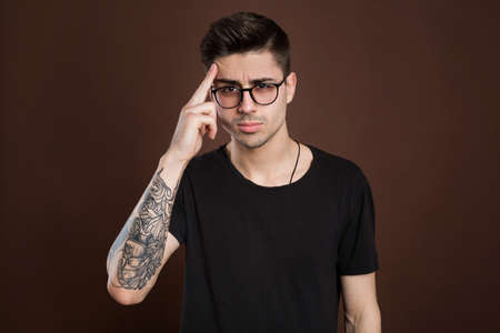 Headshot of serious thoughtful middle aged man tries to remember something in his mind, keeps fore finger on temple, keeps eyes shut, isolated over brown background, wears fashionable clothing.の写真素材