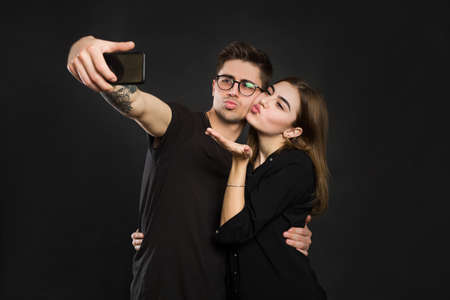 Happy young loving couple making selfie and smiling while standing against black background.