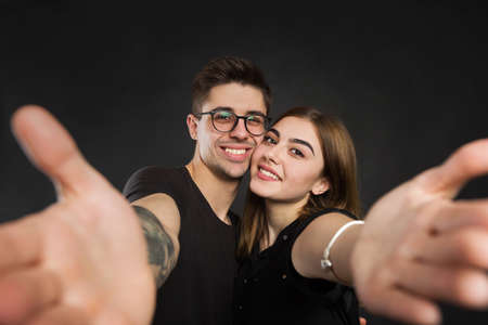 Happy young loving couple making selfie and smiling while standing against black background.の写真素材