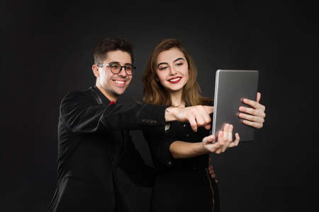 Happy couple pointing finger at digital tablet isolated on black background.