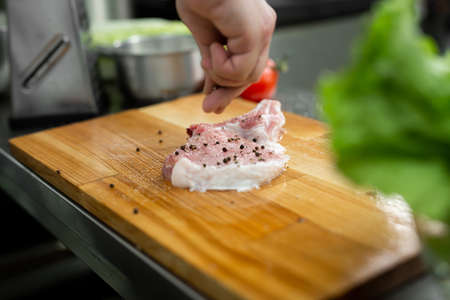 Chef peppering raw beef steak. Professional cook seasoning juicy meat with pepper, salt and herbs before grill.の写真素材