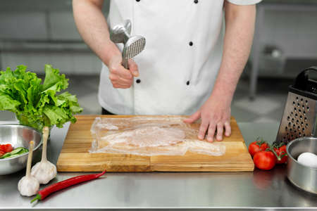 Cook beating a chicken breast with a hammer, close-up. Diet, healthy low-calorie food, weight loss concept.の写真素材