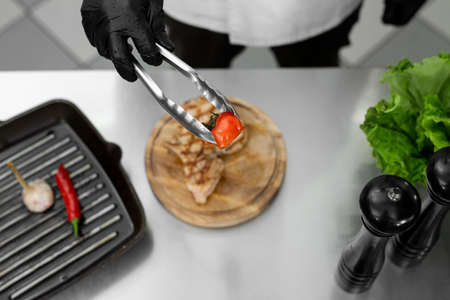 Close-up of the chefs hand as he puts a tomato from the grill on a plate with tongsの写真素材