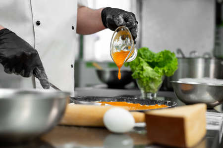Cooking pizza. Close-up of the chefs hand pouring sauce over the pizza doughの写真素材
