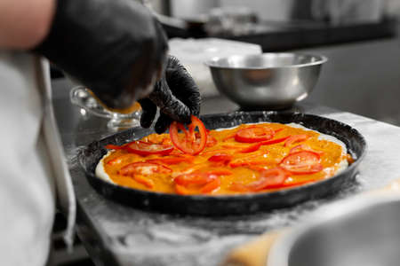 Cooking pizza. Close-up of the chefs hand spreading slices of tomato on the doughの写真素材