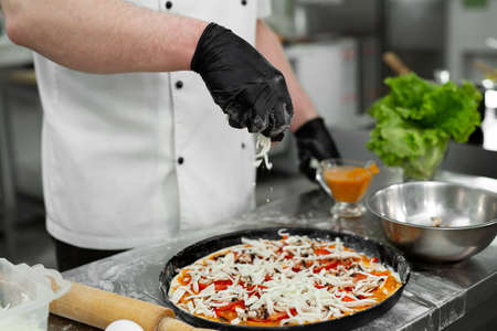 Cooking pizza. Close-up of the chefs hand sipping pizza with grated cheese before bakingの写真素材
