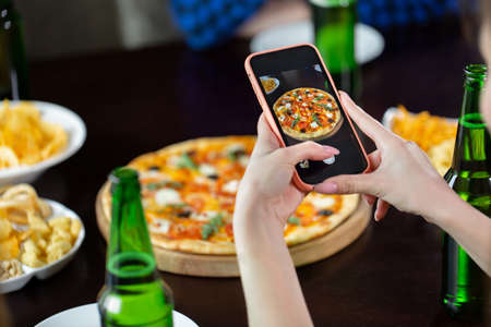 Woman taking photo of pizza with smart phone.の写真素材