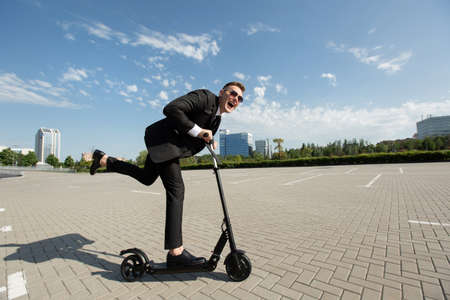 Young handsome businessman in a suit rides an electric scooter around the city and laughsの写真素材