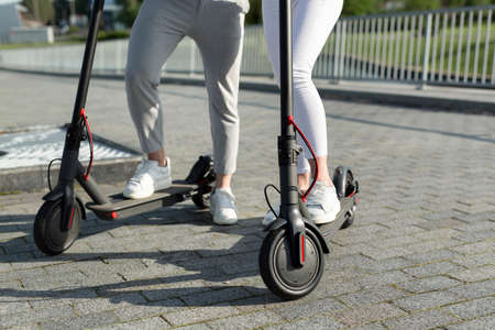 A couple of men and women are walking in the Park and standing near electric scooters