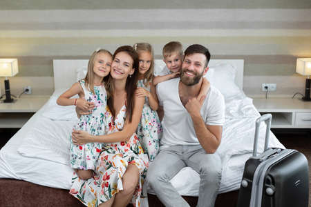 Young family: parents with children sit on the bed in the hotel and laugh. Traveling with children
