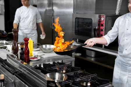 Chef cooking with flame in a frying pan on a kitchen stove.