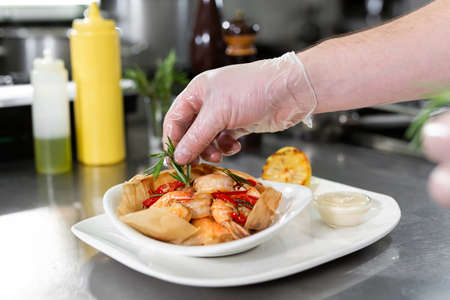 Beautiful man chef preparing dish with shrimps at table in kitchen.