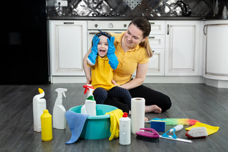 Happy mother and her daughter put on rubber gloves and enjoy cleaning, having fun together.の写真素材