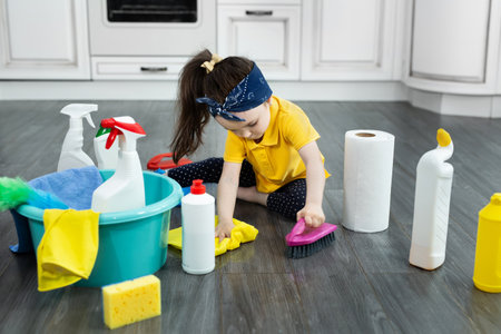 Little girl plays with detergents and a brush on the kitchen floor while cleaningの写真素材
