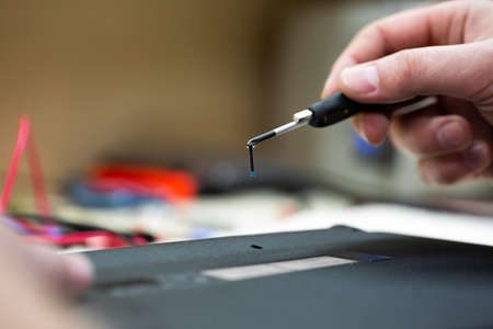 Close-up of a male engineer repairing a laptop in the workshop, disassembling the laptop cover with a screwdriver.の写真素材