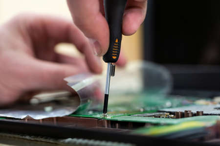 Young male tech or engineer repairs electronic equipment in research facility. A man disassembles a computer with a magnetic screwdriver.の写真素材