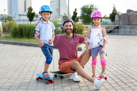 Father with his children, son and daughter, skate in the park, smile and look at the cameraの写真素材