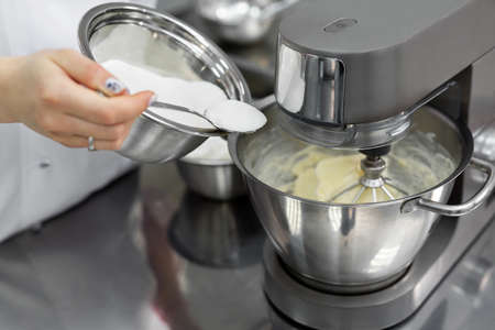 Pastry chef in the kitchen adds sugar to the kitchen machine, mixer