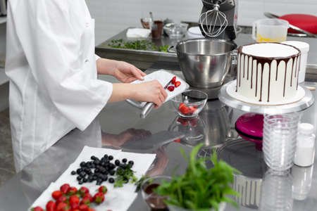 Pastry chef cuts strawberries to decorate the cake.