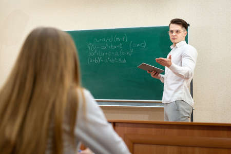 Young student with glasses and a tablet answersat the blackboard