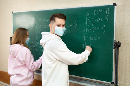Group of students with face mask writing on the board in the classroom during pandemic.の写真素材