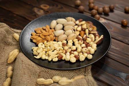 Mixture of nuts in a black plate on a brown wooden background