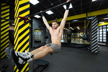 Young man flexing abdominal muscles on pull-up bar in gym.