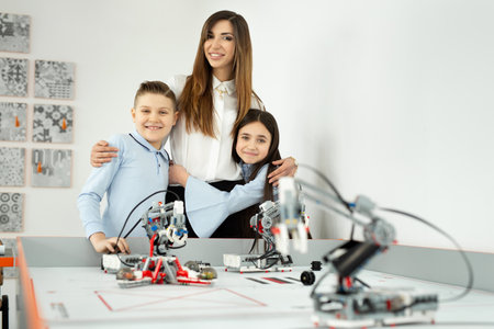 Young beautiful mother with her son and daughter pose at the school of robotics with robots from the constructorの写真素材