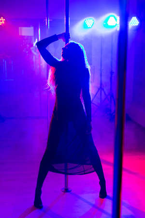 Pole dance. Young slender sexy woman dancing on a pole in the interior of a nightclub with light and...