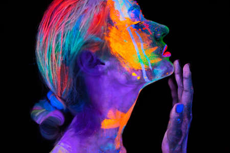 Beautiful young woman in neon light. Portrait of a model with fluorescent makeup posing in UV light with colorful makeup.の写真素材
