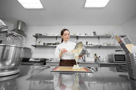 Pastry chef woman pours the dough on a baking sheet with parchmentの写真素材