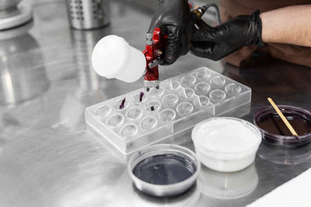 Close-up of the hands of a male pastry chef who sprays food paint with a pastry airbrush in the...