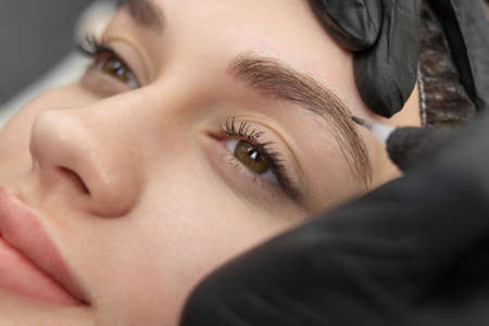 Concept of microblading eyebrows. The cosmetologist performs the procedure of permanent makeup of...