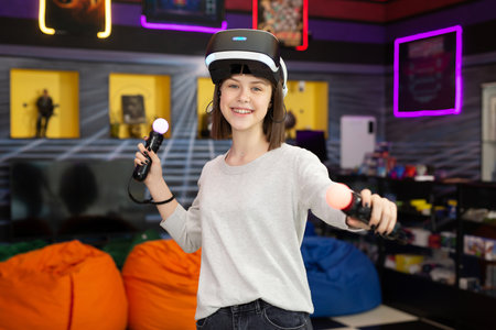 Child, a teenage girl playing on a game console in virtual reality glasses shooting a game with a remote control gun in a game club. VR.の写真素材