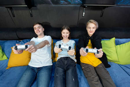 Group of friends of teenagers, boys and girls playing video games on a console in a game club