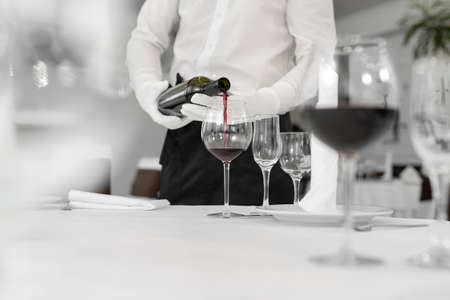 Male waiter in white gloves pours red wine into a glassの写真素材