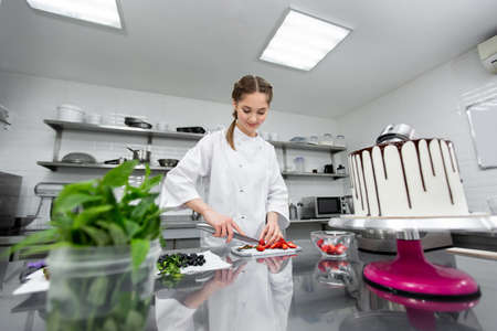 Pastry chef cuts strawberries to decorate the cake.