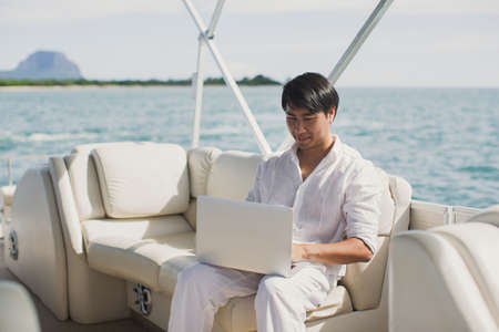 Businessman working with computer on a boat, nice outdoor office.の写真素材