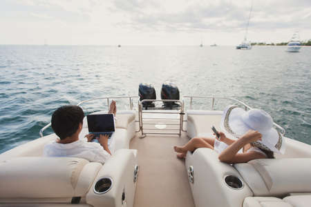 Handsome man and woman on deck of yacht with mobile phone and laptop.の写真素材